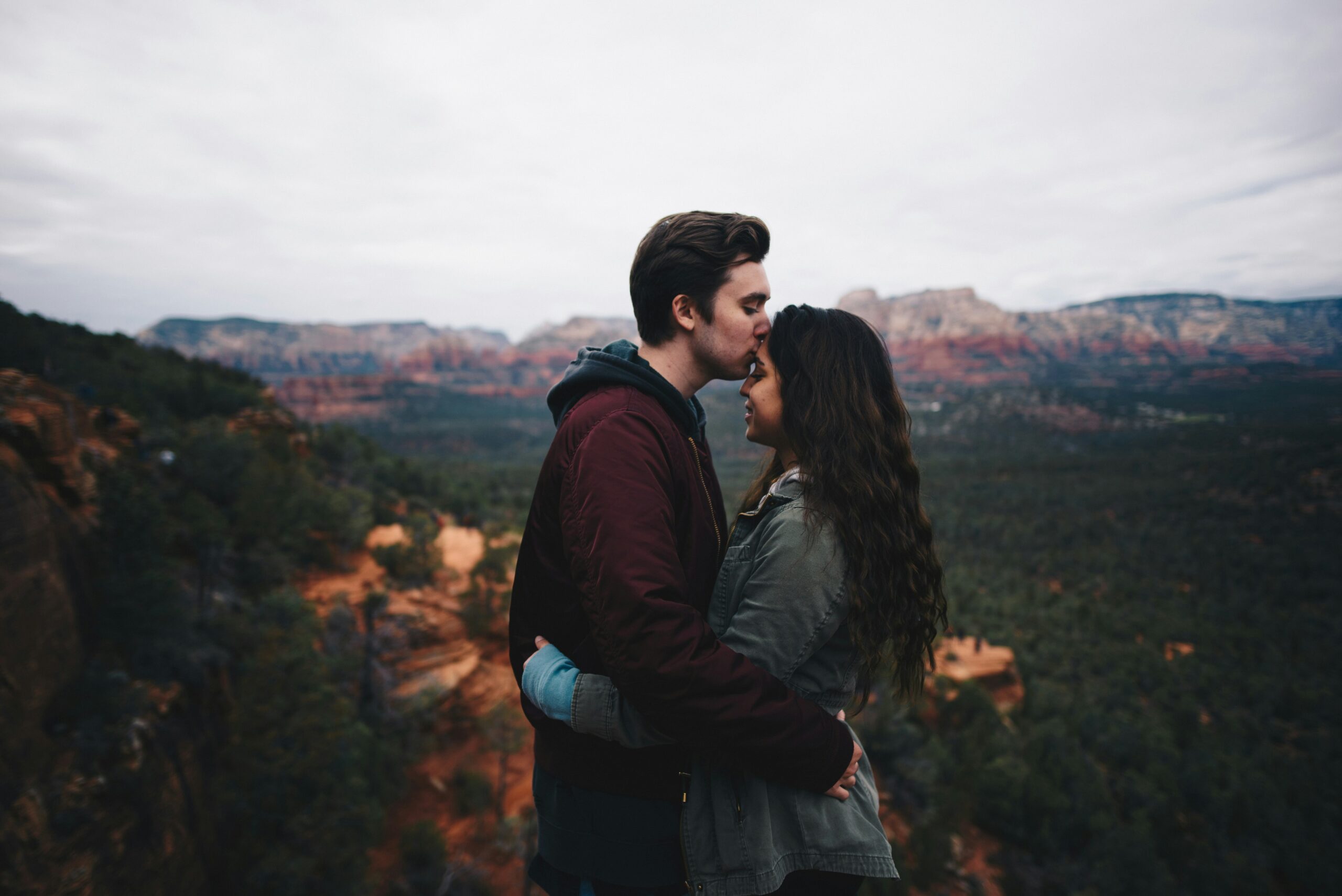 A man kissing a woman on the forehead in front of a nature scape.